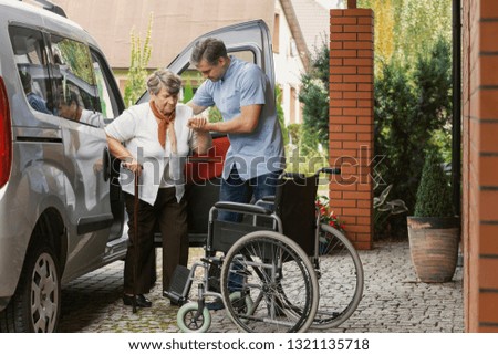 Senior woman getting out of the car with the help of a nurse