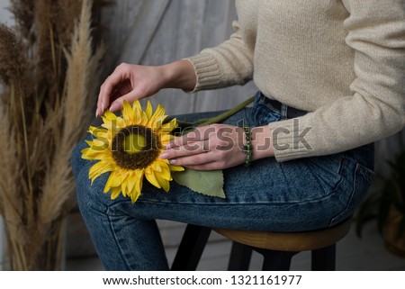 the girl has a jade bracelet, the girl is holding an artificial sunflower flower, the girl is sitting on a chair and holding a sunflower (horizontally, dark toned)