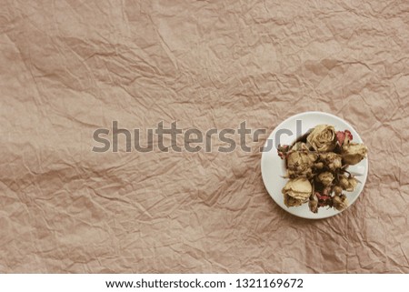 Dry roses in white cup on a brown paper background. Author processing, film effect.
