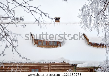 Winter time. Roof of a low-rise wooden village house with windows covered the snow and icicles