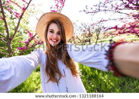 Pretty happy easy going woman making selfie smiling and laughing, wearing straw hat and elegant white top 