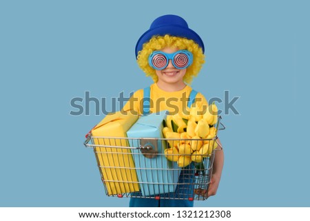 Child, sale, spring. Child in yellow,  blue colors, with a shopping cart with yellow tulips, packages.  Free space. Advertisement. 
Waist up, thin, facing camera, studio, blue background.