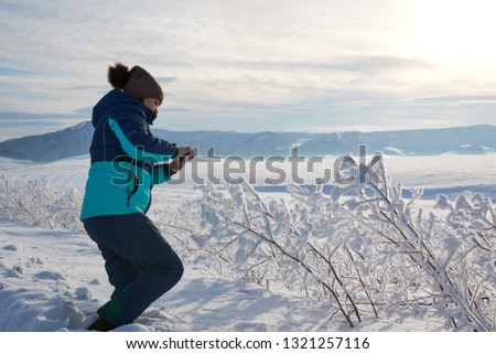 Woman taking a picture of the view with a mobile phone. Field and forest, mountains covered with snow. Blue sky.