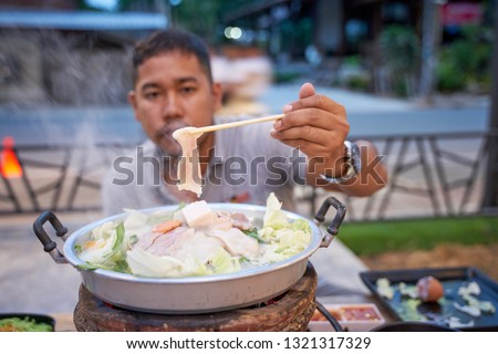 An adult man clamps Thai barbecue pork (Moo-Ka-Ta)  - famous Thai local food with need to do own cooking - food photography concept