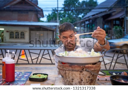 An adult man clamps Thai barbecue pork (Moo-Ka-Ta)  - famous Thai local food with need to do own cooking - food photography concept