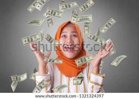 Portrait of happy successful young Asian billionaire muslim woman smiling happily under rain of money. Wealth investment economic concept