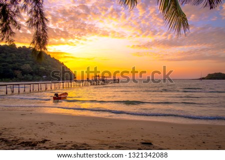 Wooden pier stretches to the sea with a small boat  in the sunset against orange sky.Beautiful tropical beach for travel in holiday relax time