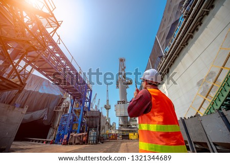 foreman, supervisor, port controller, loading master in charge of working in the dock at workplace, control and communication to the teamwork by walkie talkie radio for job done in the same direction Royalty-Free Stock Photo #1321344689