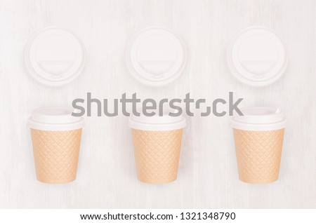 Set of three ribbed coffee kraft paper cups and blank cap on light wood board, top view. Mockup for branding identity, advertising and design concept.