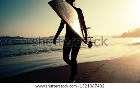 Surfer girl walking with surfboard on the beach at sunrise