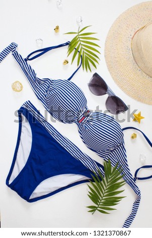 Bikini swimsuit with tropical plant,straw hat on white background. Overhead view of woman's swimwear and beach accessories. Striped swimsuit and sunglasses.Top view.Beach relaxation. Vacation concept.