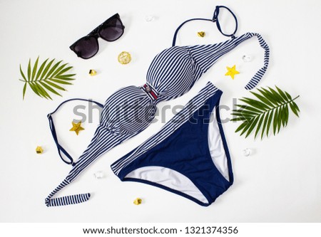 Bikini swimsuit with tropical plant,straw hat on white background. Striped swimsuit and sunglasses.Top view. Beach relaxation. Vacation concept.
 Top view essential travel items. Set of trip stuff.