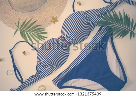 Bikini swimsuit with tropical plant,straw hat on white background. Overhead view of woman's swimwear and beach accessories. Striped swimsuit and sunglasses.Top view.Beach relaxation. Vintage style.