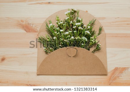 Opened envelope with white flowers arrangements on wooden background, top view. Festive greeting concept. Beautiful flowers white chamelaucium in postal envelope with heart.