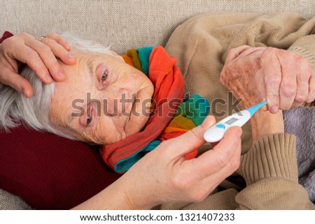 Close up picture of sick elderly woman resting on the sofa, caregivers hand holding her hands - seasonal influenza
