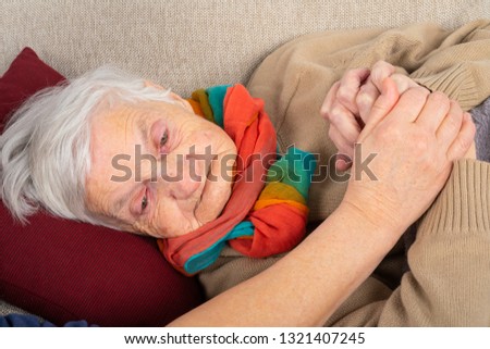 Close up picture of sick elderly woman with fever resting on the sofa, caregivers hands holding her
