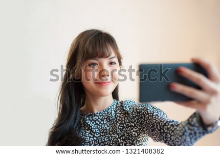 A pretty Asian girl is smiling and holding a mobile phone to take selfies.