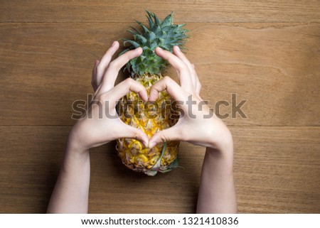 Ripe pineapple with various gestures of women hand make heart shape on wooden background.