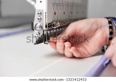 Close-up of female hands filling thread in modern embroidery machine on bright blurred white copy space background. Industrial embroidery, commercial production and high quality results concept.