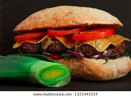 Closeup of delicious fresh homemade burger with lettuce, cheese, onions and tomatoes on dark background