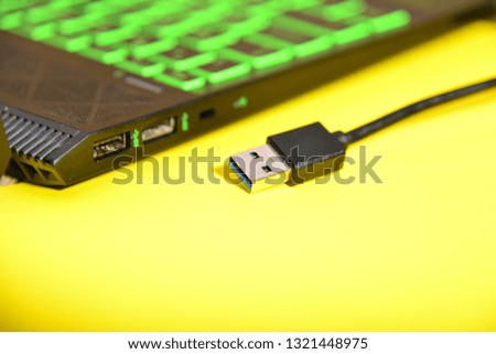 USB cable lies near the laptop on a yellow background.