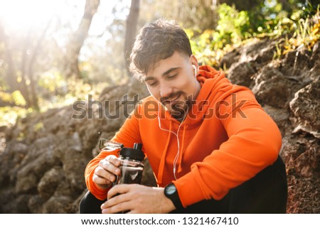 Picture of handsome young sports fitness man runner outdoors in park drinking water.