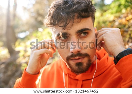 Picture of handsome young sports fitness man runner outdoors in park listening music with earphones.