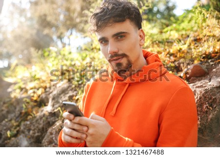 Picture of handsome young sports fitness man runner outdoors in park using mobile phone.