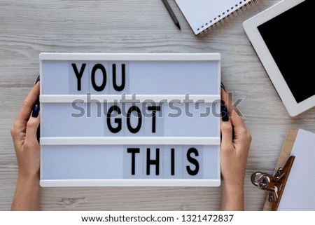 Female hands hold modern board with text 'You got this'. Feminine workspace. Business concept. Overhead, top view, from above. Flat lay.