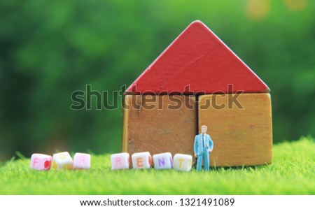 Photo Red Top House from Wooden Block Toy at Fresh Green Grass for Rent with blur Tree and Yellow Flower with Standing Mini Figure Businessman toy
