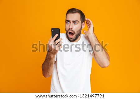 Photo of terrified man 30s in casual wear looking at mobile phone with fear isolated over yellow background Royalty-Free Stock Photo #1321497791
