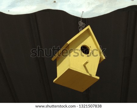 spring yellow birdhouse hanging on a black wall background