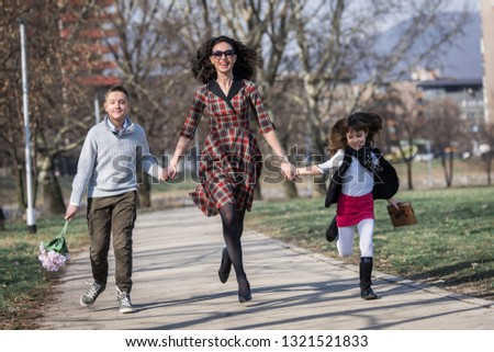 Mother together with son and daughter take a walk through the park casually walking enjoying the sunny day