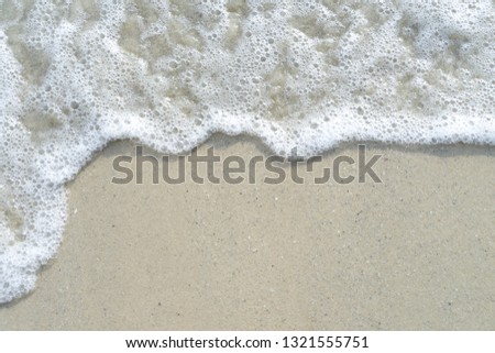 Soft wave of the sea on the sandy beach with white clean foam water surf. Top view with copy space.