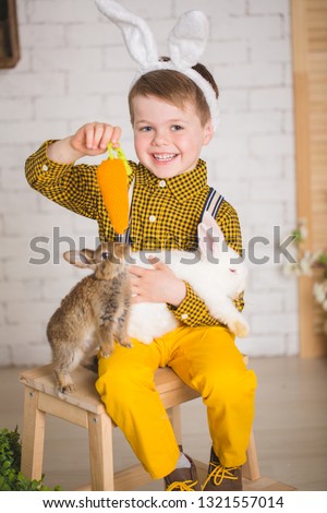 Stylish boy in yellow pants and with ears of the Easter Bunny. Toddler posing in studio in Easter scenery with two bunnies