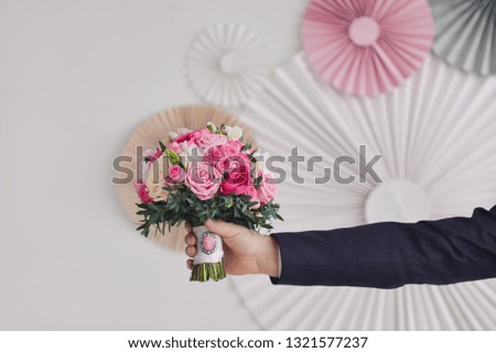man's hand of the groom holds the wedding bridal bouquet of pink roses with a brooch against the background of corrugated wedding decor