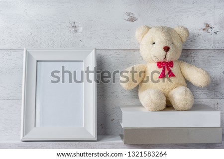 white blank photo frame on wooden shelf and wall, decorate with stack of books and teddy bear doll