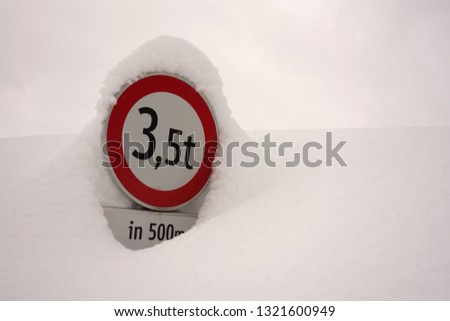 Round traffic sign covered by snow with cloudy sky in the background