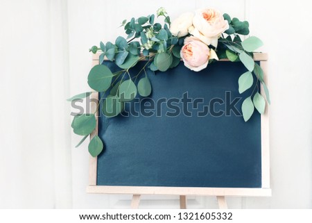 Blank wedding chalkboard sign mockup scene. Floral garland of green eucalyptus branches and apricot English roses flowers. Rustic birthday party decoration. Wooden easel with welcome board.