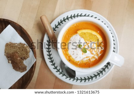 Light lunch delight: orange, carrot and pumpkin soup in a mug with slice of soda bread and a wooden spoon on the wooden table