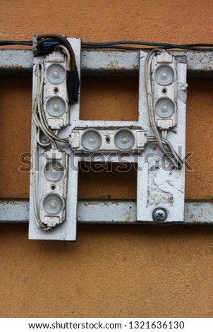 A background photo with an old broken signboard with light bulbs. Letter H