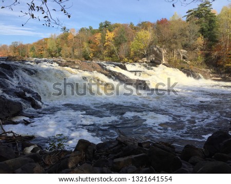 Beautiful waterfall on fast shallow river in the autumn park in green and yellow forest trees and deep blue sky background. Landscape