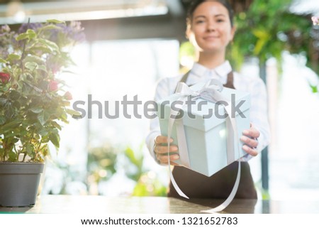 Contemporary florist or shop assistant holding white box tied up with silk ribbon over workplace