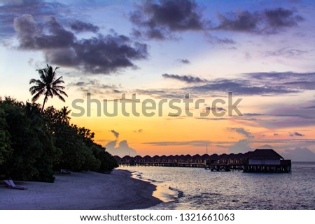 Silhouette of Villas and palm tree in the lagoon in tropical island in Maldives during sunset time with purple sky