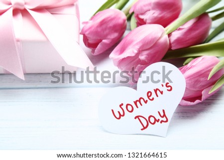 Text Women's Day with pink tulip flowers and gift box on wooden table