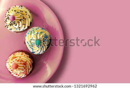 Top view on homemade colorful cupcakes with white cream on a green ceramic plate. Pink rose background. Birthday Party. Greeting card. Banner with sweet cupcakes with free space for text message