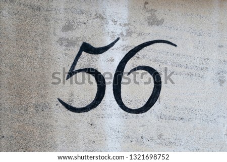 Vinatge style house number 56 painted in black on white wall.