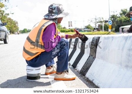 worker painting black-white lines on concrete barrier. Road work and construction.