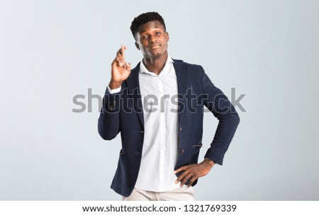 Handsome african american man wearing a jacket with fingers crossing and wishing the best. Making a wish. on isolated grey background