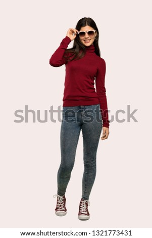 A full-length shot of a Teenager girl with turtleneck with glasses and smiling over isolated background
